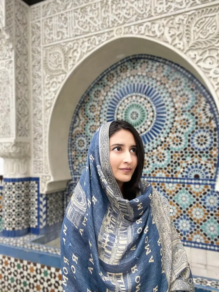 Blogger is wearing a headscarf in front of a beautiful wall with blue and gold Islamic architecture at the Gran Mezquita de París, France