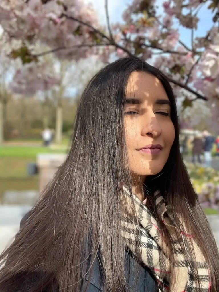 Blogger is standing in the shade of a cherry blossom tree with her eyes closed while inhaling to ease her travel anxiety during her first solo trip to the Netherlands