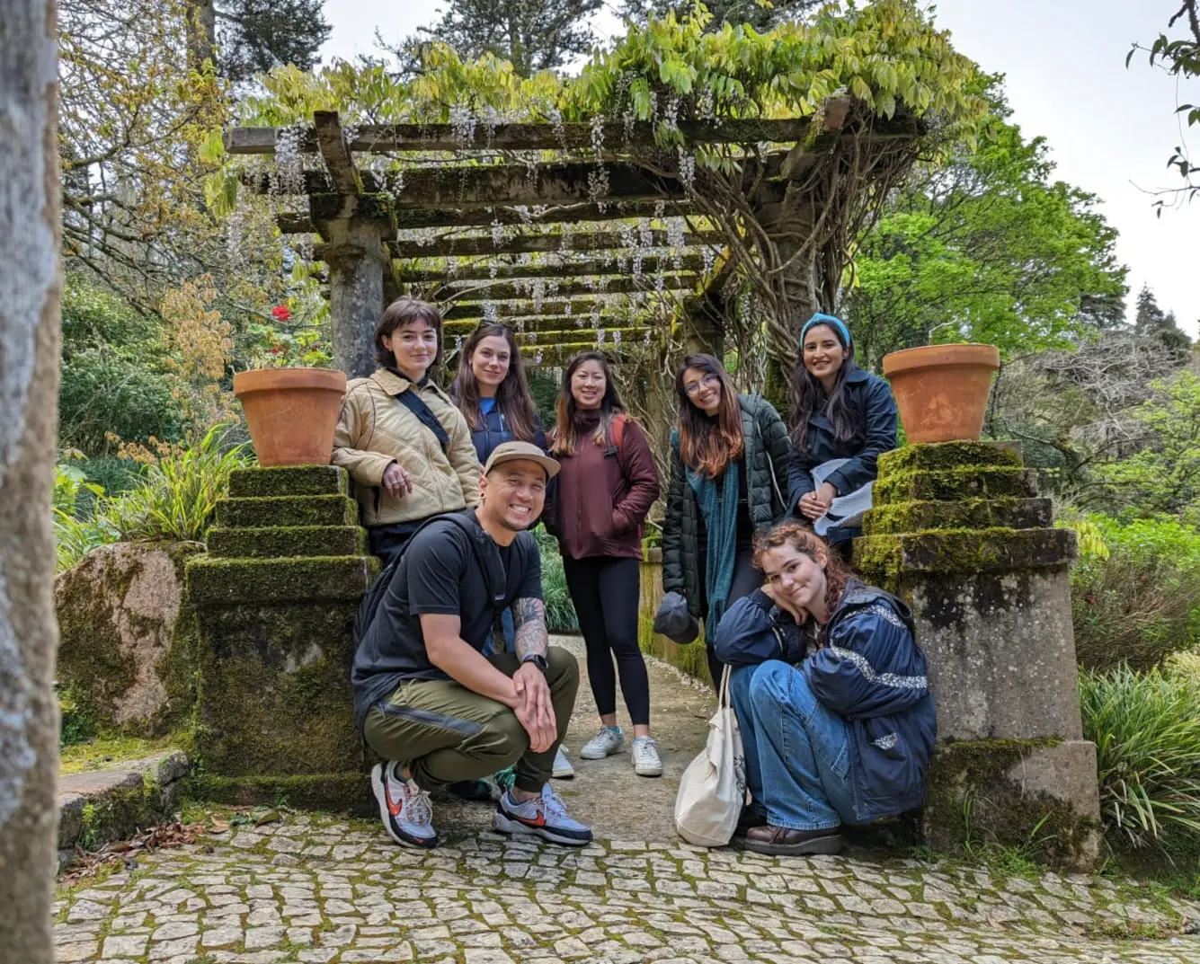 Group photo in Sintra, Portugal. 6 women and 1 man are smiling into the camera in the greenery.